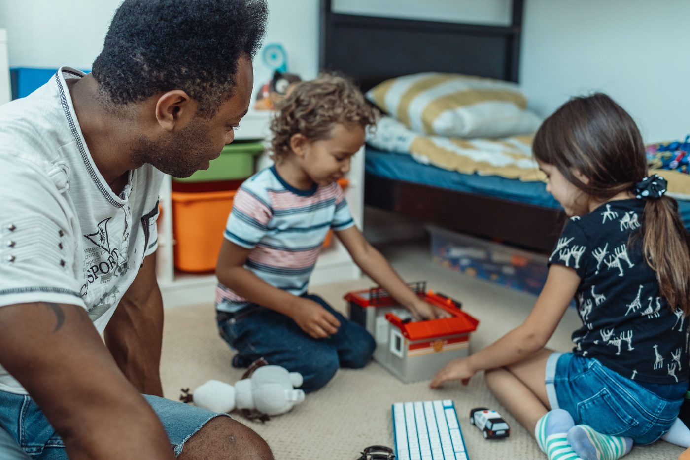 A father on the floor with two children putting toys into a bin