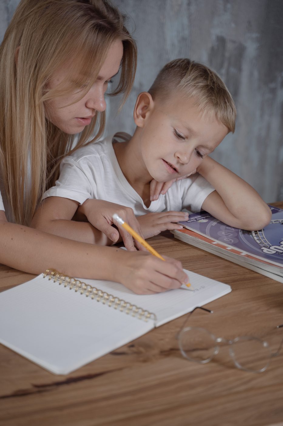 A parent sitting alongside a child working through homework at the table